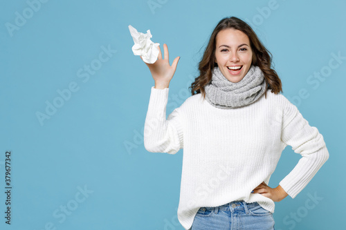 Cheerful funny young woman wearing white sweater gray scarf throwing out paper napkin isolated on blue background studio portrait. Healthy lifestyle ill sick disease treatment cold season concept. photo