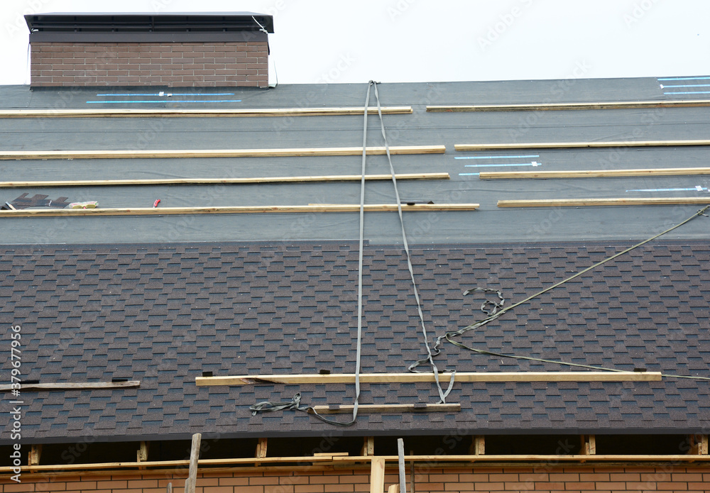 Φωτογραφία A close-up on a roof under construction with asphalt shingles installation on felt paper or underlayment with safety roof harness and ropes that were left by roofing contractors