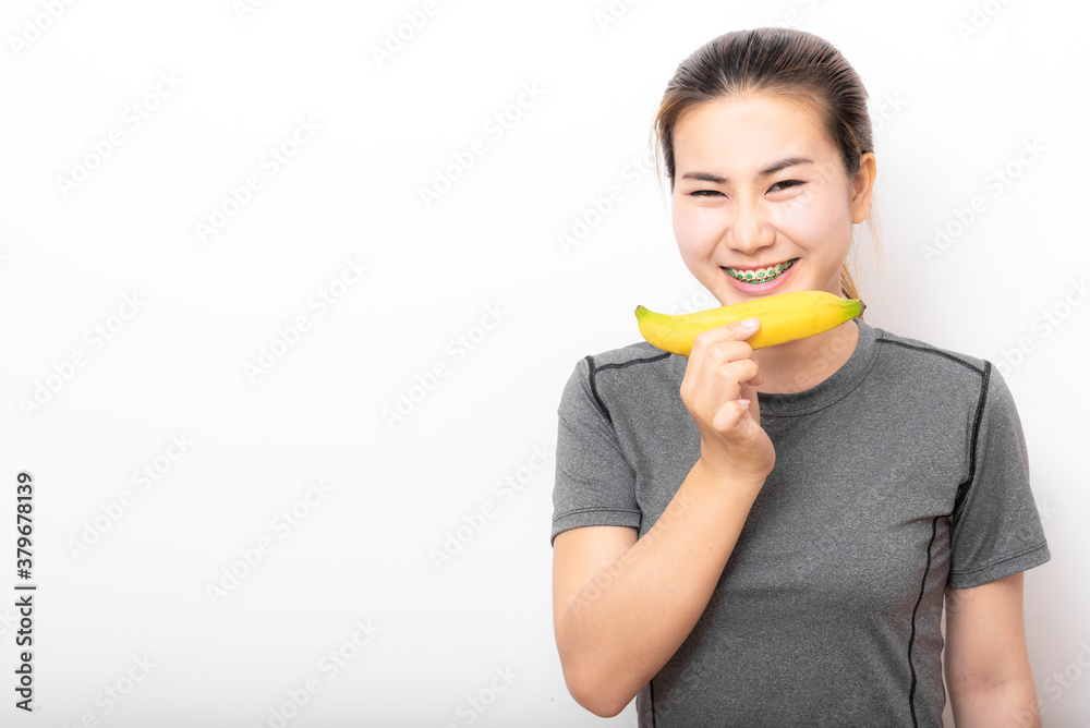 Happy Asian woman with detal braces holding banana on white background Happy Asian woman with detal braces holding banana on white background