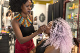 A black makeup artist making up a young girl with pink crochet hair style.