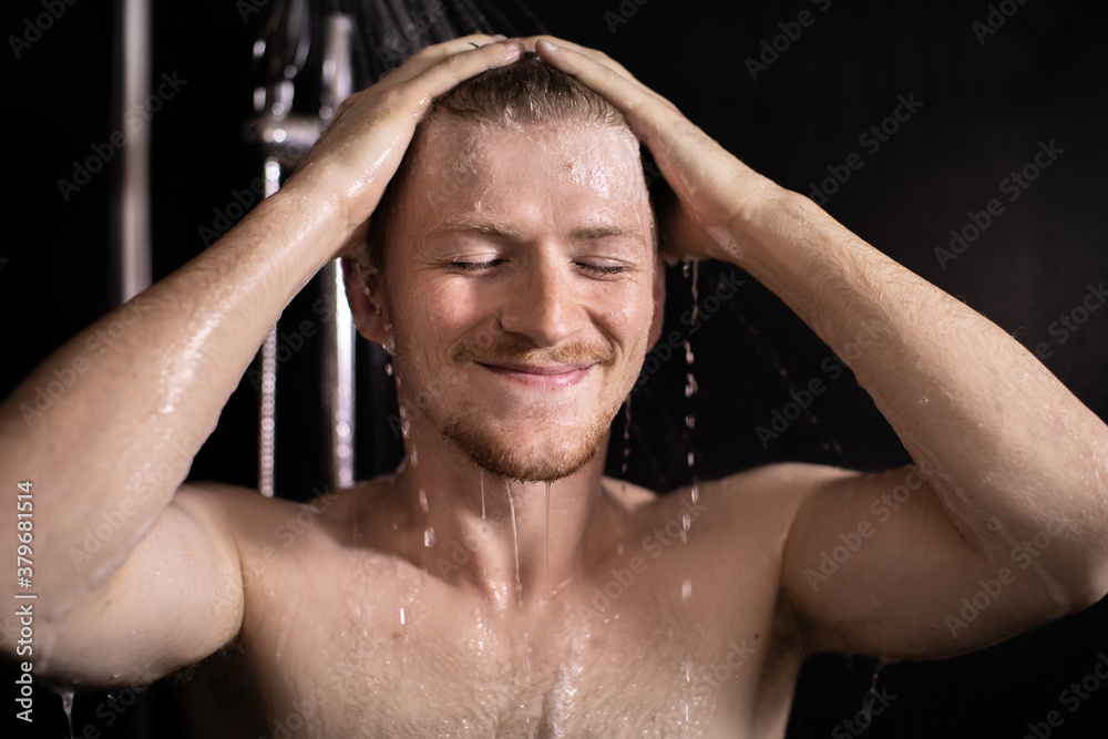 Happy beautiful man standing under stream of hot water in bathroom, taking shower, young smiling guy enjoying showering. Lifestyle, beauty, personal care, shower systems, relaxing time concept Happy beautiful man standing under stream of hot water in bathroom, taking shower, young smiling guy enjoying showering. Lifestyle, beauty, personal care, shower systems, relaxing time concept