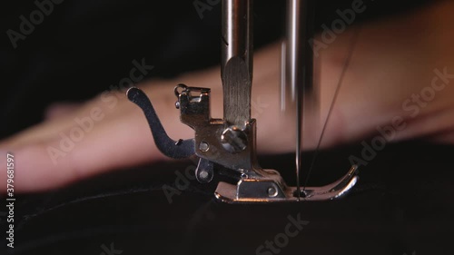 woman sews on a white sewing machine with black threads on a black fabric close up