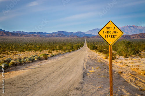 Sign stating Not A Through Street on a very long dirt road in the desert