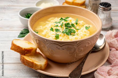 Italian stracciatella egg drop soup with parmesan cheese and parsley in bowl on rustic wooden background
