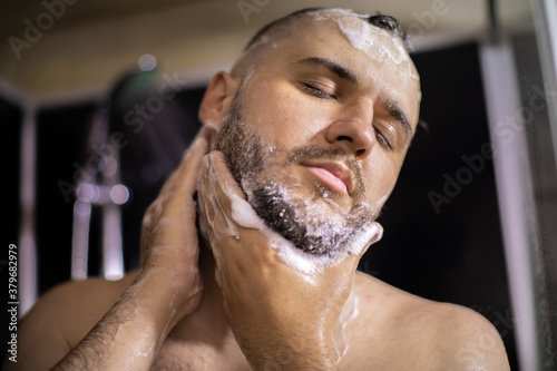 Close up view of handsome man with closed eyes washes face, beard in bathroom, taking shower. Lifestyle, beauty, personal care, relaxing time, young guy enjoying showering, Body, skin and hair hygiene