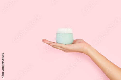 Mano femenina sosteniendo un pote frasco de crema sobre un fondo rosa pastel liso y aislado. Vista de frente y de cerca. Copy space. Concepto: Belleza