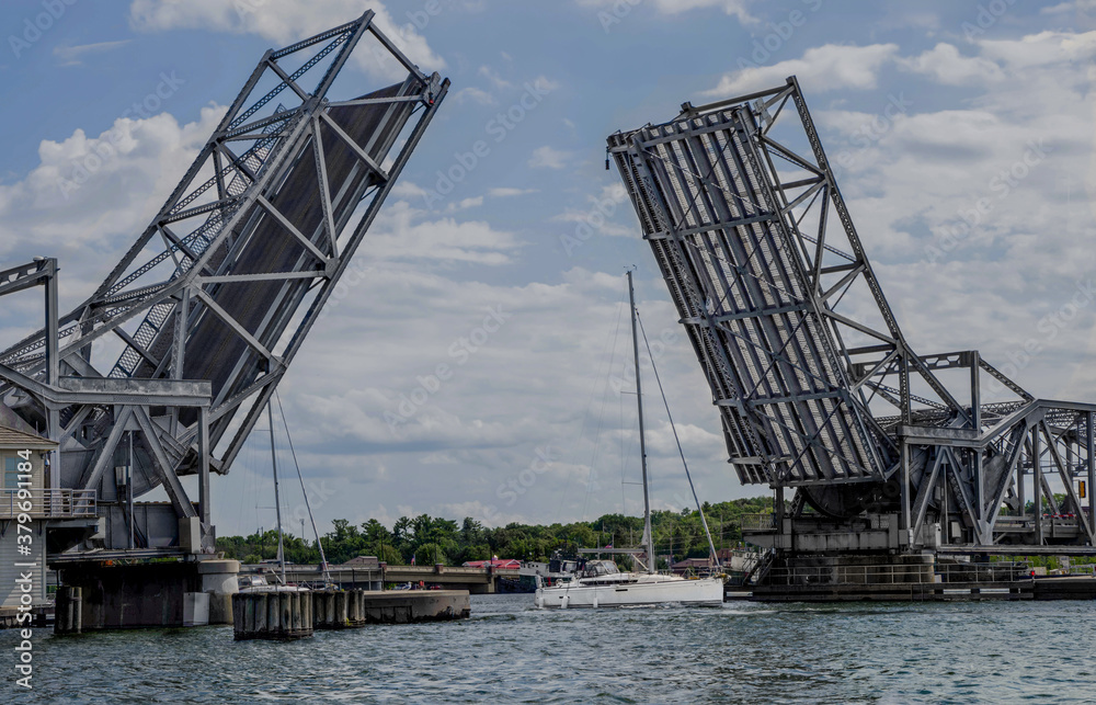 Drawbridge Up:  A bridge designed to separate at the middle raises its two sides to allow passage of a sailboat through the harbor at Sturgeon Bay, Wisconsin.
