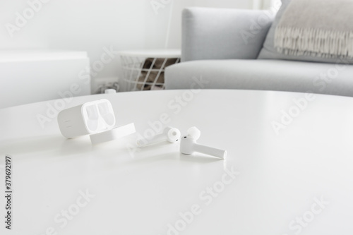 White wireless earbuds with charging case on a wooden table. © Finmiki