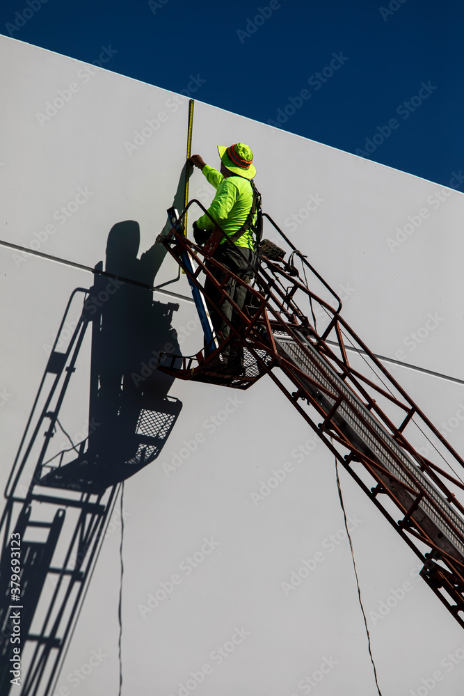 Painter wearing a hat on a ladder casting a shasow on a white commercial building