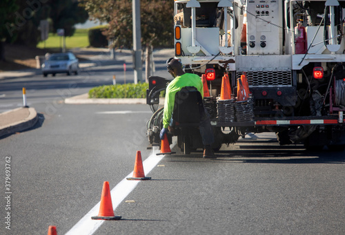 Piant striping truck with seat at the back bumper where a worker sits and places traffic cones onto the street. The truck also has an electonic traffic directional arrow photo