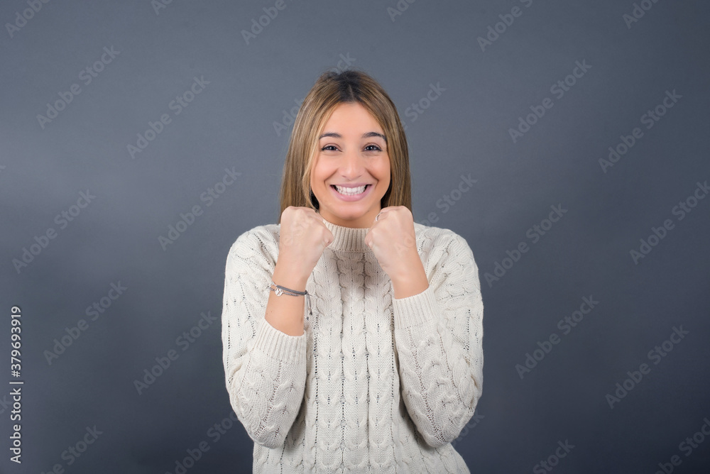 Beautiful blonde young woman wearing white sweater feeling confident against gray studio background. Beautiful blonde young woman wearing white sweater feeling confident against gray studio background.