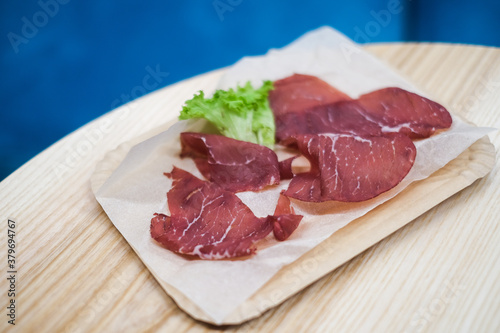 Meat smoked jerky - raw meat sausage meat. Close up view on tasty sliced Chicken basturma on paper plate on a wooden background . Beer snack. Pastirma photo