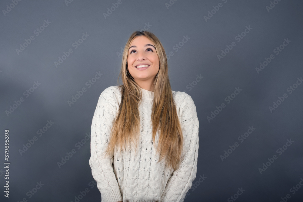 Beautiful blonde young woman wearing white sweater feeling confident against gray studio background. Beautiful blonde young woman wearing white sweater feeling confident against gray studio background.
