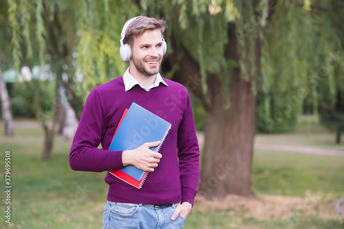 Modern College Student standing in park listening music with earphone and reading book, students life