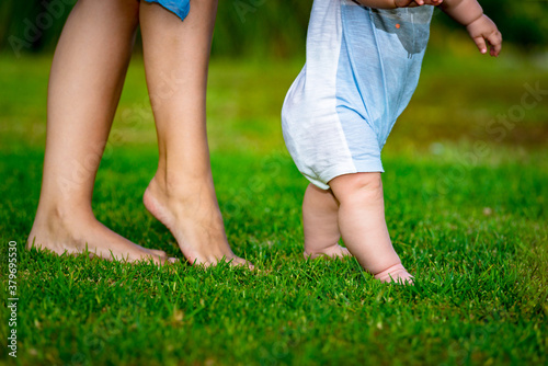 Two children legs on the green grass and female legs behind at the blurred background