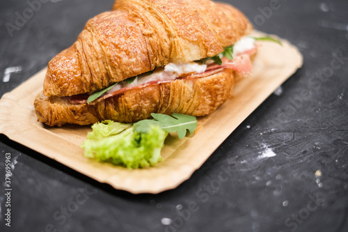 Croissant with ham and cheese arugula and lettuceon, in a paper plate top view