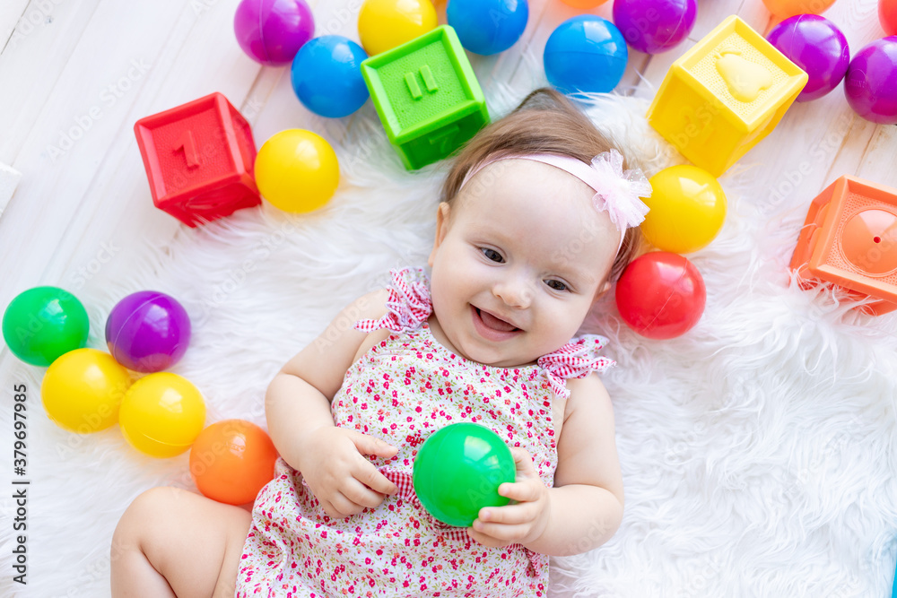 a beautiful little baby girl is lying in red clothes on a white Mat among toys balls and cubes a beautiful little baby girl is lying in red clothes on a white Mat among toys balls and cubes