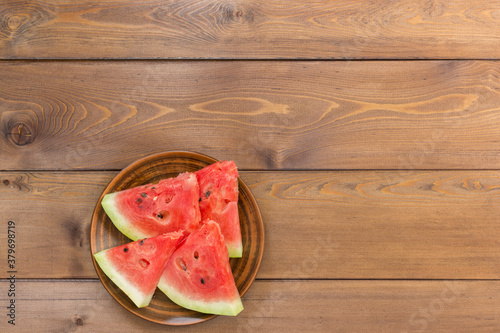 Four slices of ripe fresh watermelon in a clay dish on a brown wooden table