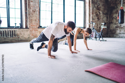 Strong caucasian male and female couple in love enjoying workout together keeping healthy lifestyle  positive woman having workout with professional trainer standing in plank training body endurance