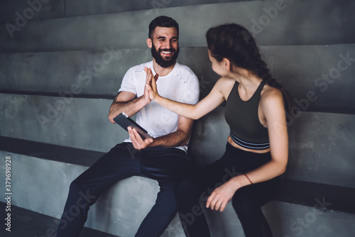 Happy caucasian female in active wear giving high five her male trainer enjoying slimming and reaching fitness goals, smiling woman and man athletes satisfied with share content in bog about sport
