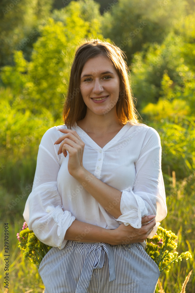 A beautiful Caucasian girl stands in a field among the yellow grass and looks at the camera smiling. Warm autumn concept A beautiful Caucasian girl stands in a field among the yellow grass and looks at the camera smiling. Warm autumn concept
