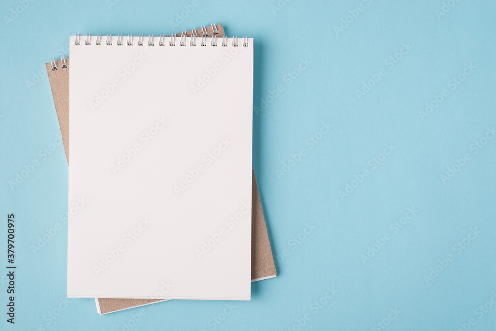 Top above overhead view flat lay photo of a blank notebook placed to the left side isolated on pastel blue color background with copyspace Top above overhead view flat lay photo of a blank notebook placed to the left side isolated on pastel blue color background with copyspace