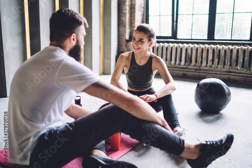 Fototapeta Naklejka Na Ścianę i Meble -  Happy young 20s woman having positive conversation with male trainer in gym discussing exercises and nutrition on consultancy, smiling couple in love satisfied with workout results share feedbacks