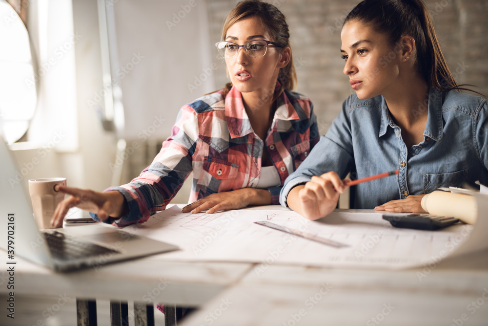 Fototapeta premium Young creative businesswomen working on blueprints in the office