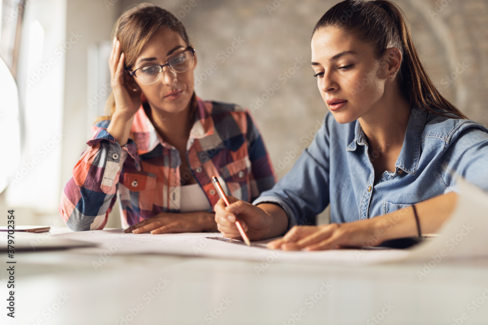 Young female architect writing something down on blueprints while working in the office Young female architect writing something down on blueprints while working in the office