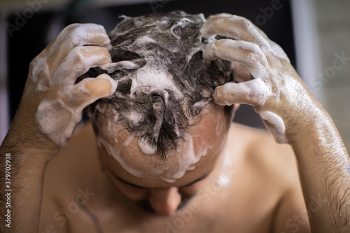 young bearded naked brunette man massaging his head in shower with shampoo foam or hair care product. Advertising for men's hair cosmetics or conditioner or antihairloss remedy photo