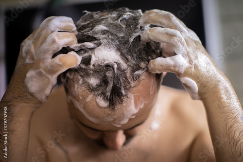 young bearded naked brunette man massaging his head in shower with shampoo foam or hair care product. Advertising for men's hair cosmetics or conditioner or antihairloss remedy