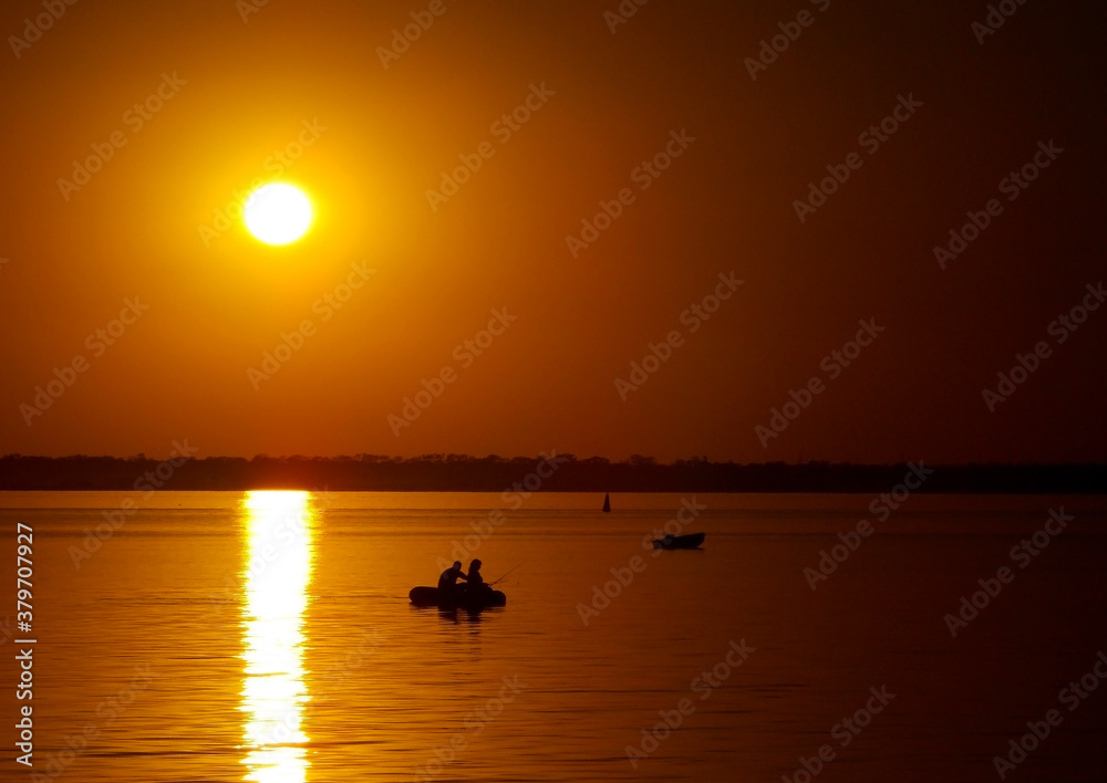 Beautiful golden sunset over the lake with silhouettes of boats with people