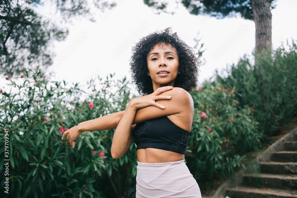 Content ethnic sportswoman stretching arm on stairs Content ethnic sportswoman stretching arm on stairs