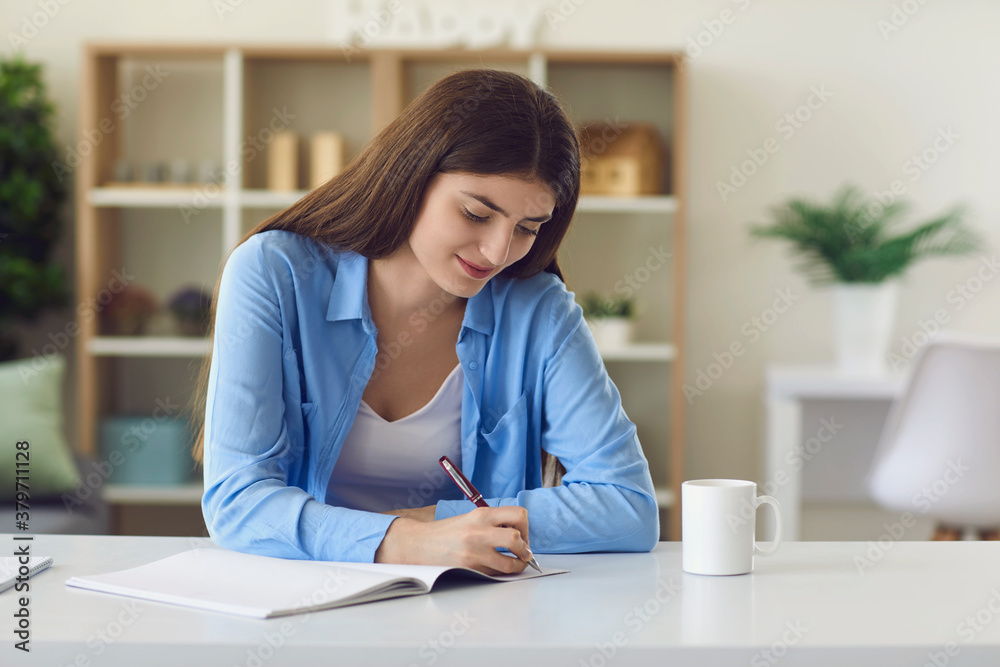 Smiling woman studying and writing down notes during online lesson on laptop Smiling woman studying and writing down notes during online lesson on laptop