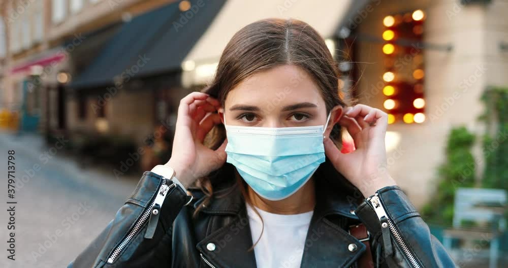 Portrait of beautiful young stylish Caucasian woman looking at camera and wearing medical mask at street. Pretty female taking on respiratory protection outdoor. Pandemic concept. Coronavirus. Portrait of beautiful young stylish Caucasian woman looking at camera and wearing medical mask at street. Pretty female taking on respiratory protection outdoor. Pandemic concept. Coronavirus.