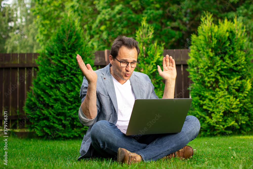 Joyful surprised middle aged businessman sits on grass works outdoors, looks with surprise at laptop screen, man happy with stock growth and higher earnings profit, winner, success concept, copy space Joyful surprised middle aged businessman sits on grass works outdoors, looks with surprise at laptop screen, man happy with stock growth and higher earnings profit, winner, success concept, copy space