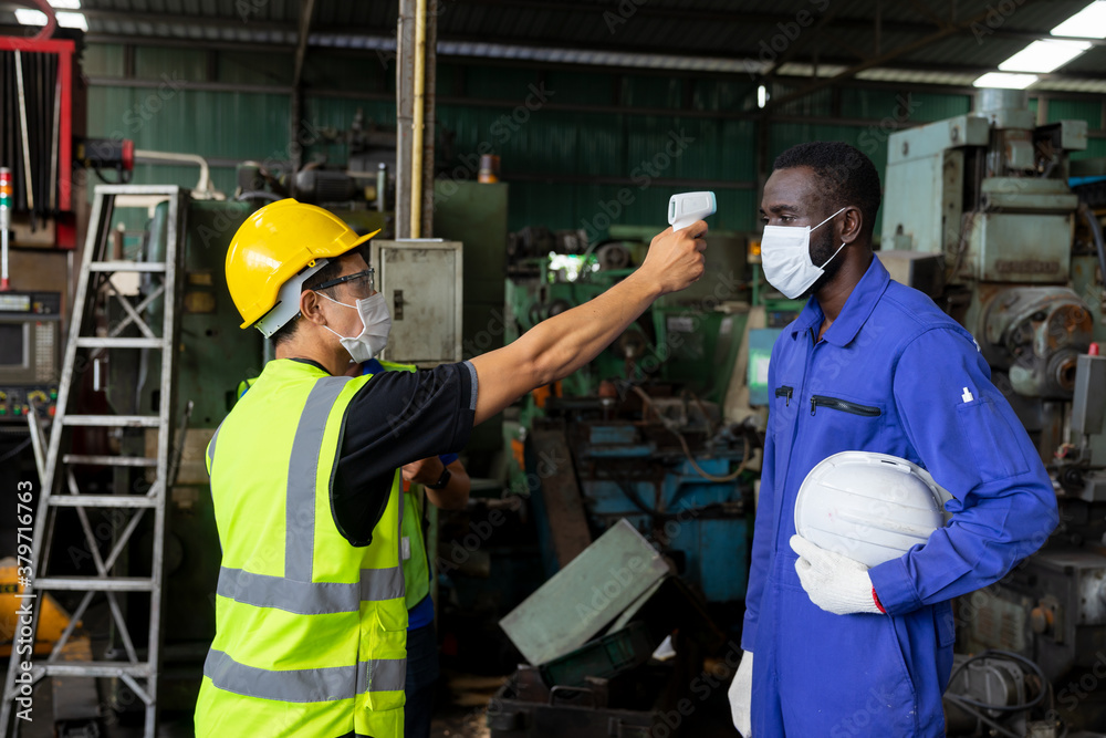 Foreman using an infrared thermometer measuring temperature to check the worker before working at manufacturing factory on business day that covid-19 coronavirus is epidemics. New normal concepts Foreman using an infrared thermometer measuring temperature to check the worker before working at manufacturing factory on business day that covid-19 coronavirus is epidemics. New normal concepts