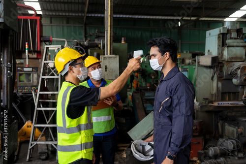 Foreman using an infrared thermometer measuring temperature to check the worker before working at manufacturing factory on business day that covid-19 coronavirus is epidemics. New normal concepts