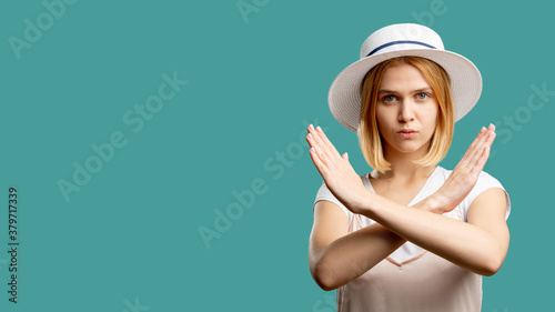 Stop sign. Forbidden gesture. Serious woman in white crossing hands looking at camera isolated on green copy space. Wrong way. No entrance. Disapproval emotion. Advertising background