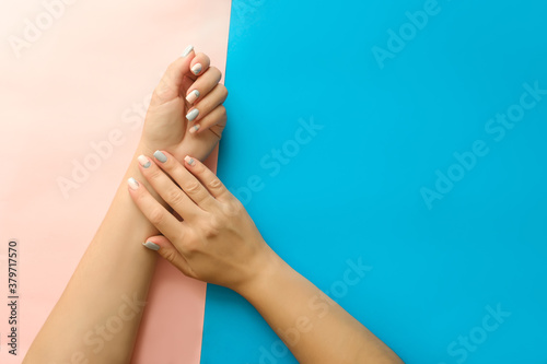 Beautiful young woman s hands with manicure on pink and blue background.