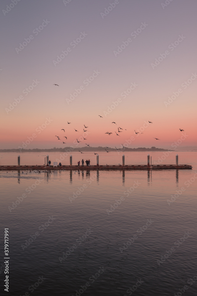 Pastel colored sunset over crabbing dock in Oregon with people and seagulls.