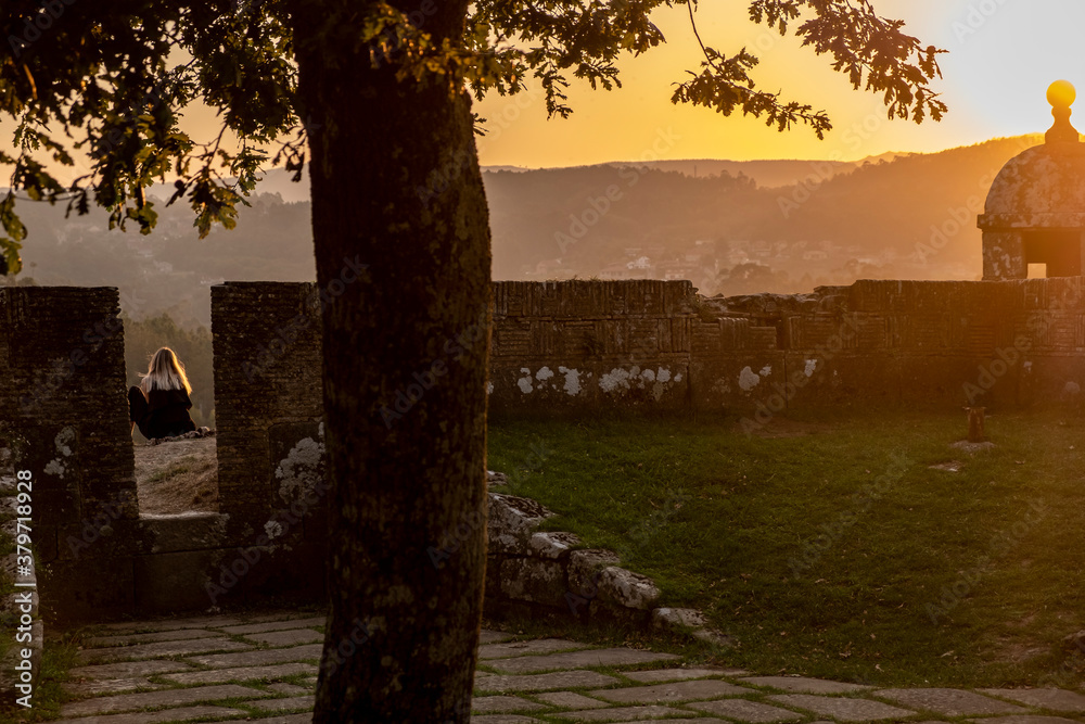 Fototapeta premium An unrecognizable girl contemplates the sunset. Walls of the fortress city of Valença do Minho. Portugal. Life style.