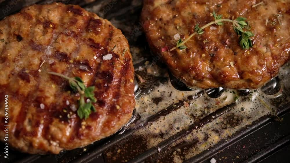Grilled hamburgers on the grill. Burger cutlet is cooked in a grill pan, thyme, steam, smoke, fire. Butter is melted. Grill food. Slow motion. Grilled hamburgers on the grill. Burger cutlet is cooked in a grill pan, thyme, steam, smoke, fire. Butter is melted. Grill food. Slow motion.
