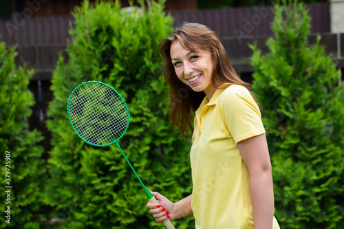 Happy smiling badminton player holding racket in hands. Young fit beautiful woman playing badminton outdoors. Sport, activity, power, confidence, energy, summer, game, leisure concept. Copy text space © Model Republic