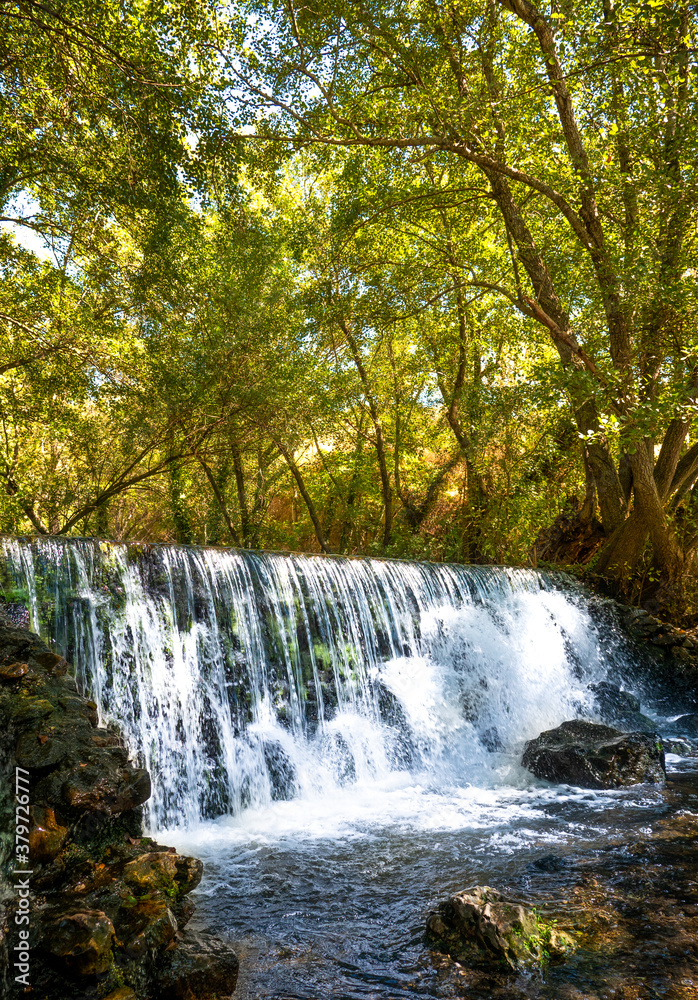 Natural waterfall called “Cascada del Hervidero” in Madrid, in the forest, with sunlight between vegetation and rocks. 