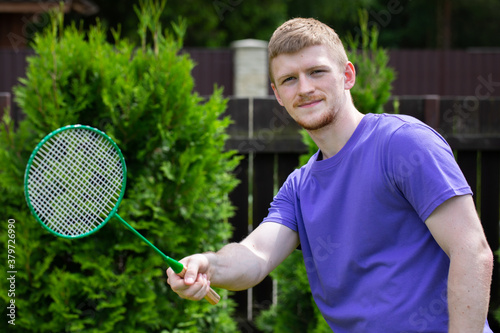 Young strong sport Caucasian man posing with badminton racket on green background. concept of amateur game of badminton, outdoor activities. © Model Republic
