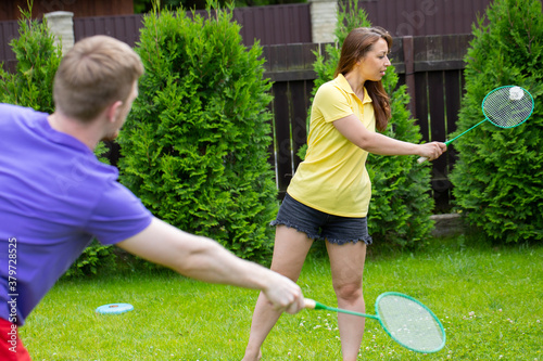 happy caucasian couple play badminton with racquets and shuttlecock on green background. concept of amateur game of badminton, outdoor activities