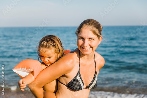 Mother carrying daughter piggyback on beach