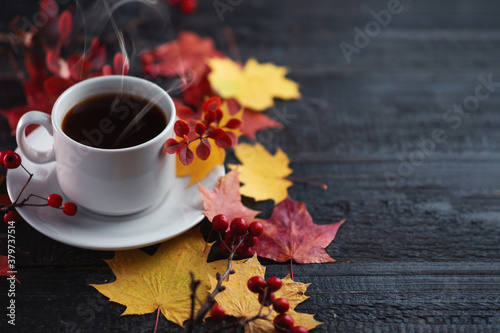 A white espresso Cup on a wooden table with yellow and red maple leaves and a barberry branch