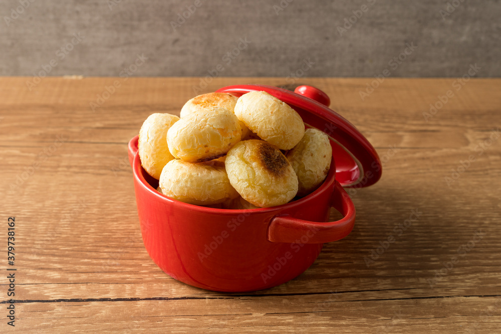 Traditional Brazilian Snack Cheese Bread in a rustic red cooking pot. On a wooden table background. with copy space